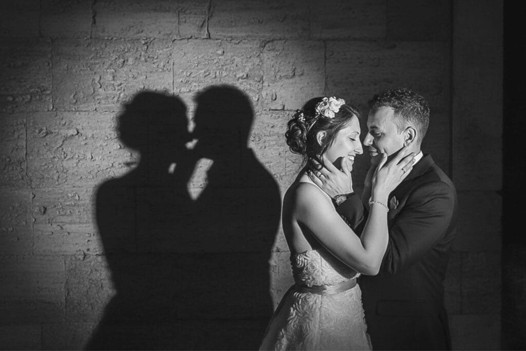 Fotografie artistică alb-negru cu umbrele mirilor pe zidul de piatră, moment intim și simbolic